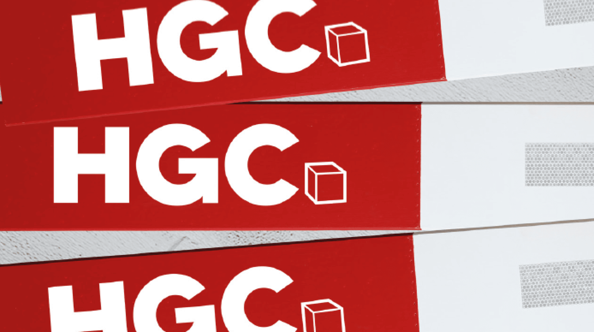 Nahaufnahme von drei schief gestapelten rot-weißen Etiketten, auf denen jeweils die fetten weißen Buchstaben HGC neben einem kleinen Würfelumriss auf der rechten Seite zu sehen sind.