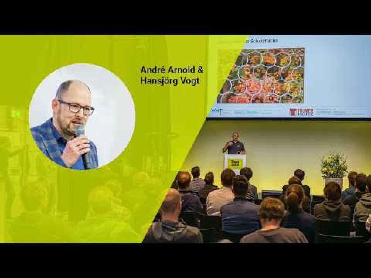 Präsentationsveranstaltung mit André Arnold, der auf einem Podium zu einem Publikum spricht; auf dem Bildschirm sind ein Bild und ein Text über Lebensmittel zu sehen. An der Seite ist sein Foto mit Mikrofon und dem Namen André Arnold & Hansjörg Vogt zu sehen.