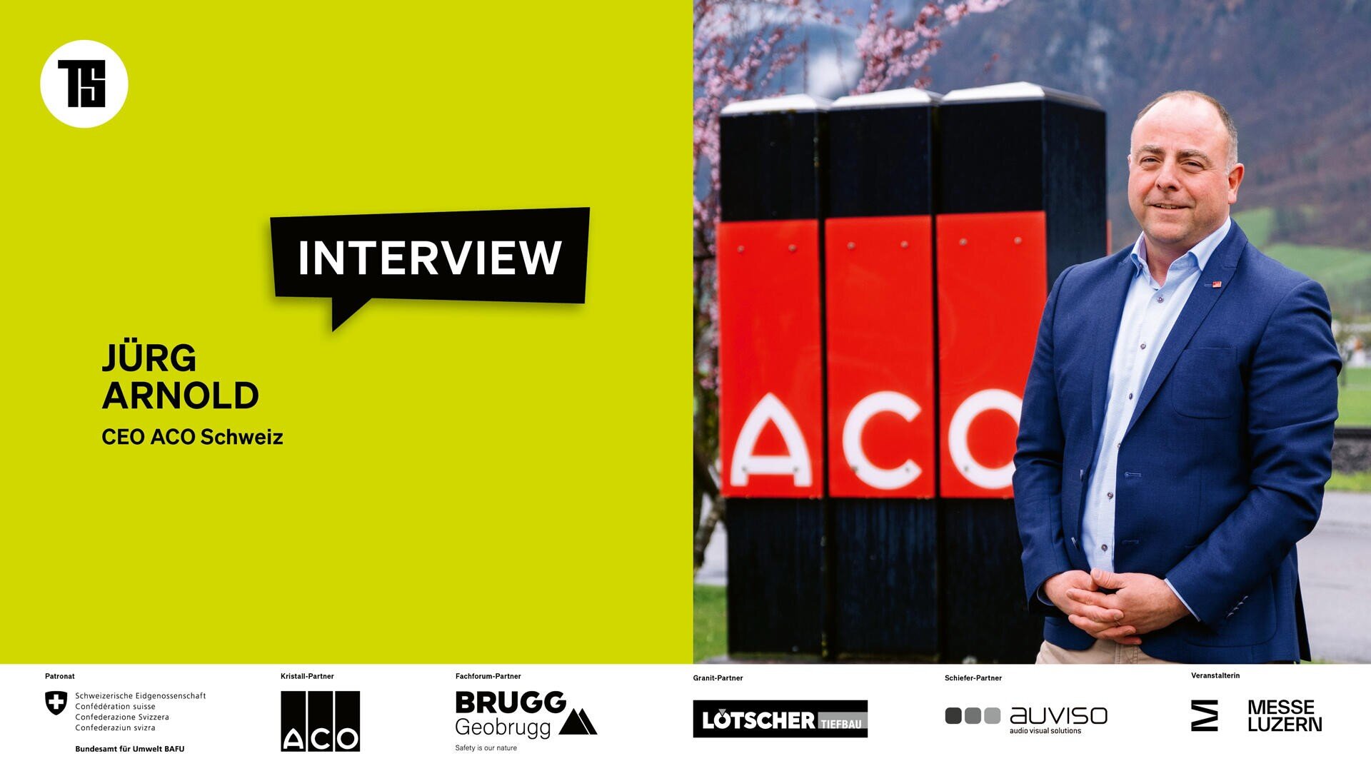 Ein Mann im Anzug steht neben einem rot-schwarzen ACO-Schild im Freien. Die linke Seite des Bildes ist gelb mit Text: INTERVIEW Jürg Arnold, CEO ACO Schweiz. Am unteren Rand erscheinen Sponsorenlogos.