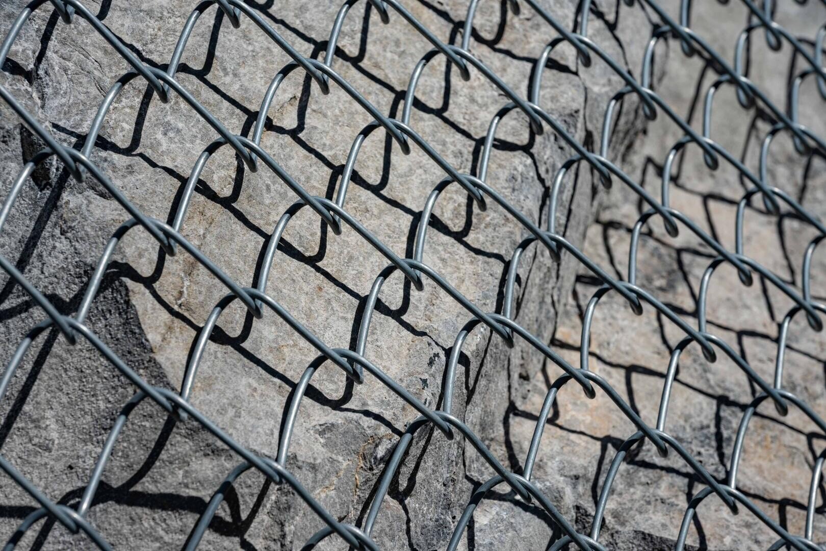 Eine Nahaufnahme von grauen Steinen, die von einem Metallgitterzaun gehalten werden und eine Gabionenwand zur strukturellen Unterstützung oder zum Erosionsschutz bilden.